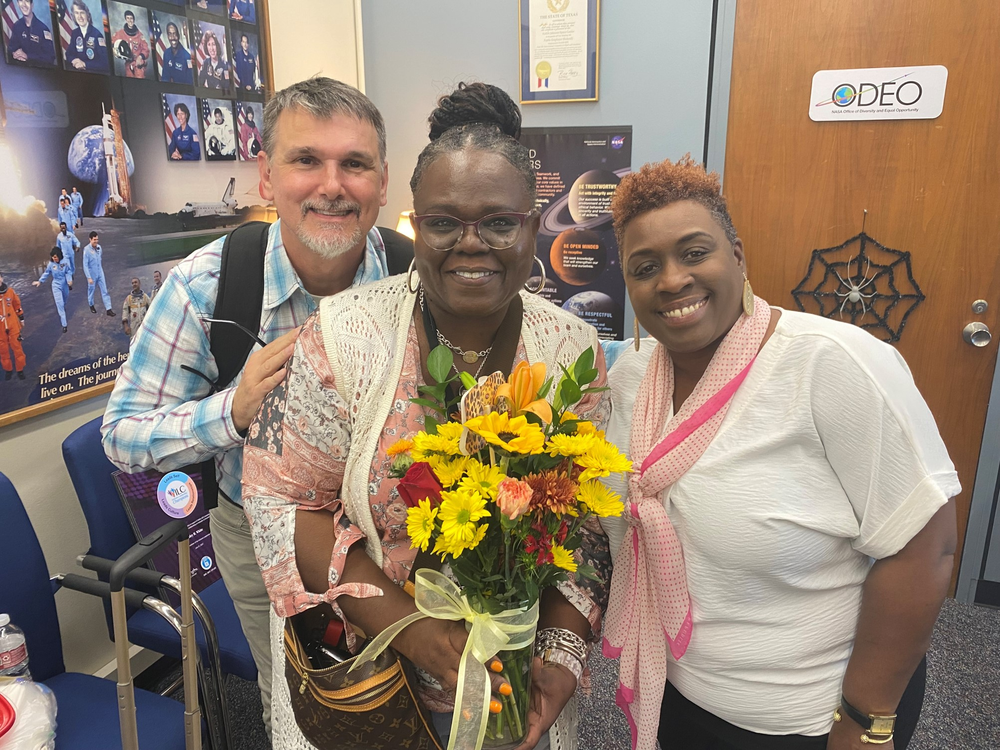 A woman receives flowers from two people in an office.